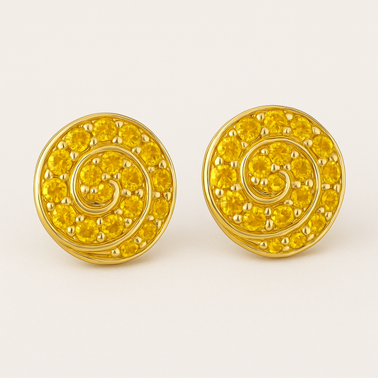 A pair of round gold stud earrings featuring a spiral design set with vibrant yellow sapphires. Each earring showcases 14 gemstones intricately arranged along a golden swirl pattern, displayed against a soft cream background.