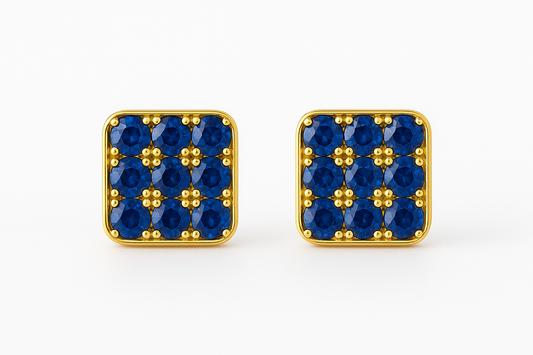 Square 18k gold stud earrings featuring a grid of vivid blue sapphires set in a rounded-edge frame, with delicate gold bead prongs accentuating each stone. Displayed on a soft cream background with a subtle reflection.