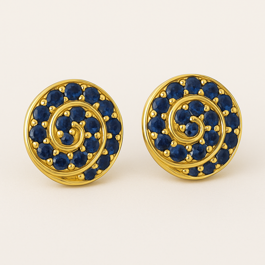 A pair of round gold stud earrings featuring a spiral design set with vibrant blue sapphires. Each earring showcases 14 gemstones intricately arranged along a golden swirl pattern, displayed against a soft cream background.
